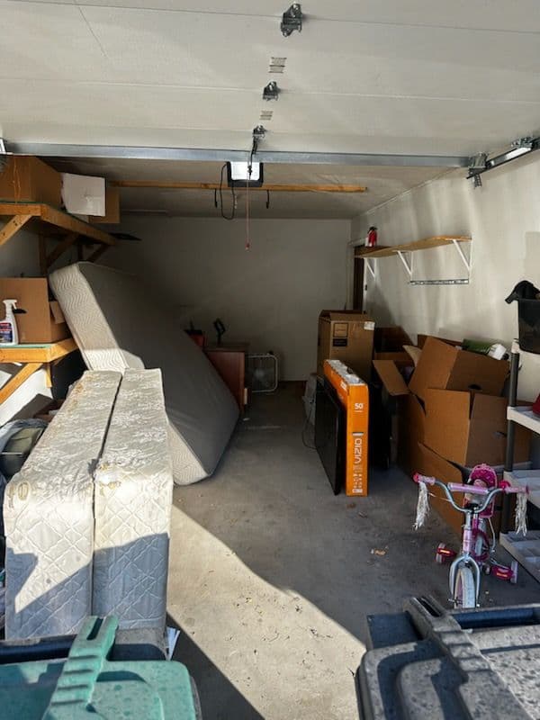 Cluttered garage interior with stacked boxes, a mattress, and a child's bike.
