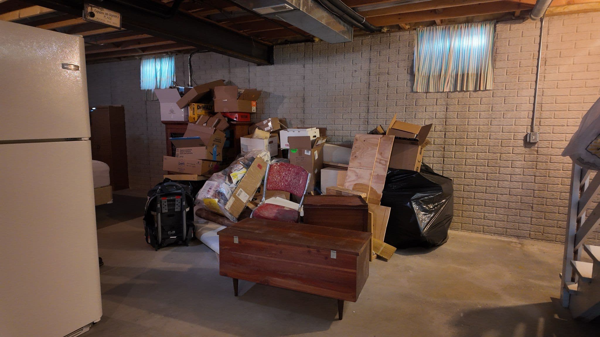 Cluttered basement with stacked boxes, furniture, and a black trash bag.