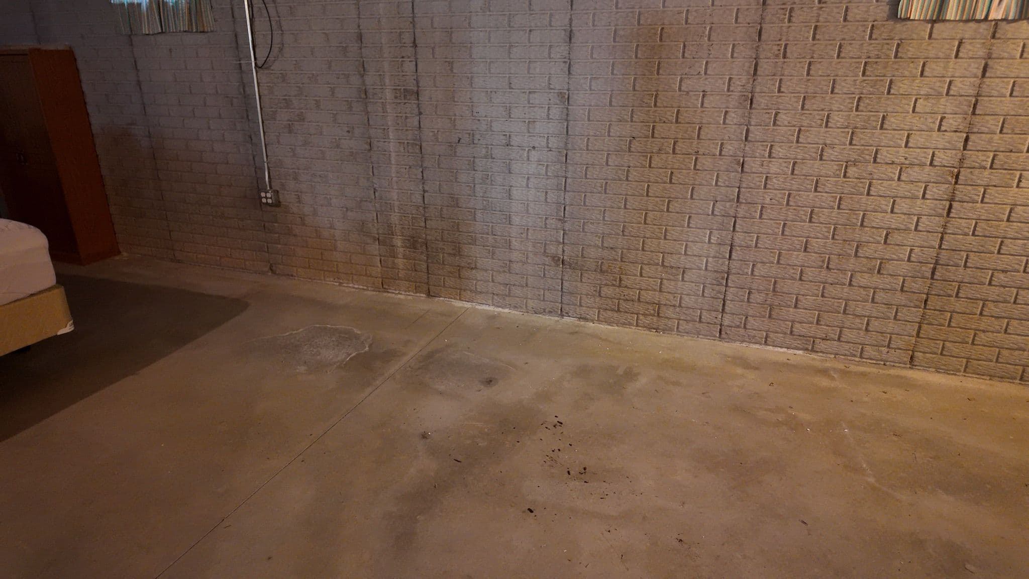 Basement with stained concrete floor and block wall, showing signs of moisture damage.